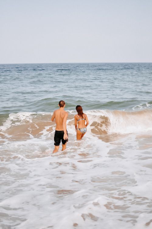 Free A young couple walks into the sea on a sunny beach day. Stock Photo