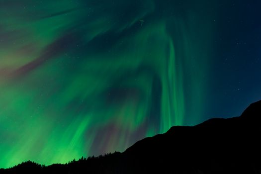A breathtaking view of the Northern Lights casting vibrant green hues over a mountain silhouette at night.