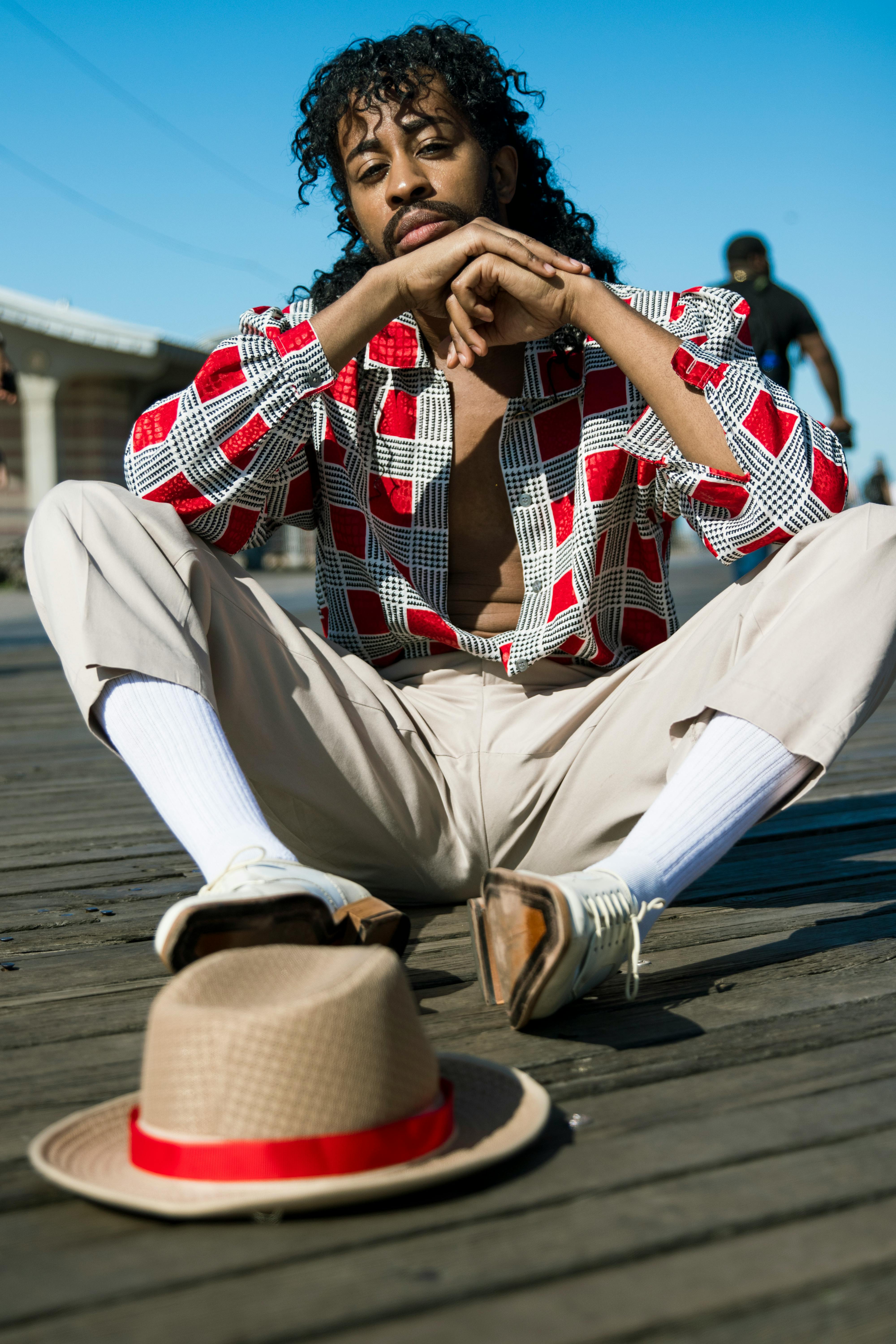 Stylish man sitting on a boardwalk in casual outfit, with a hat on the wooden planks.