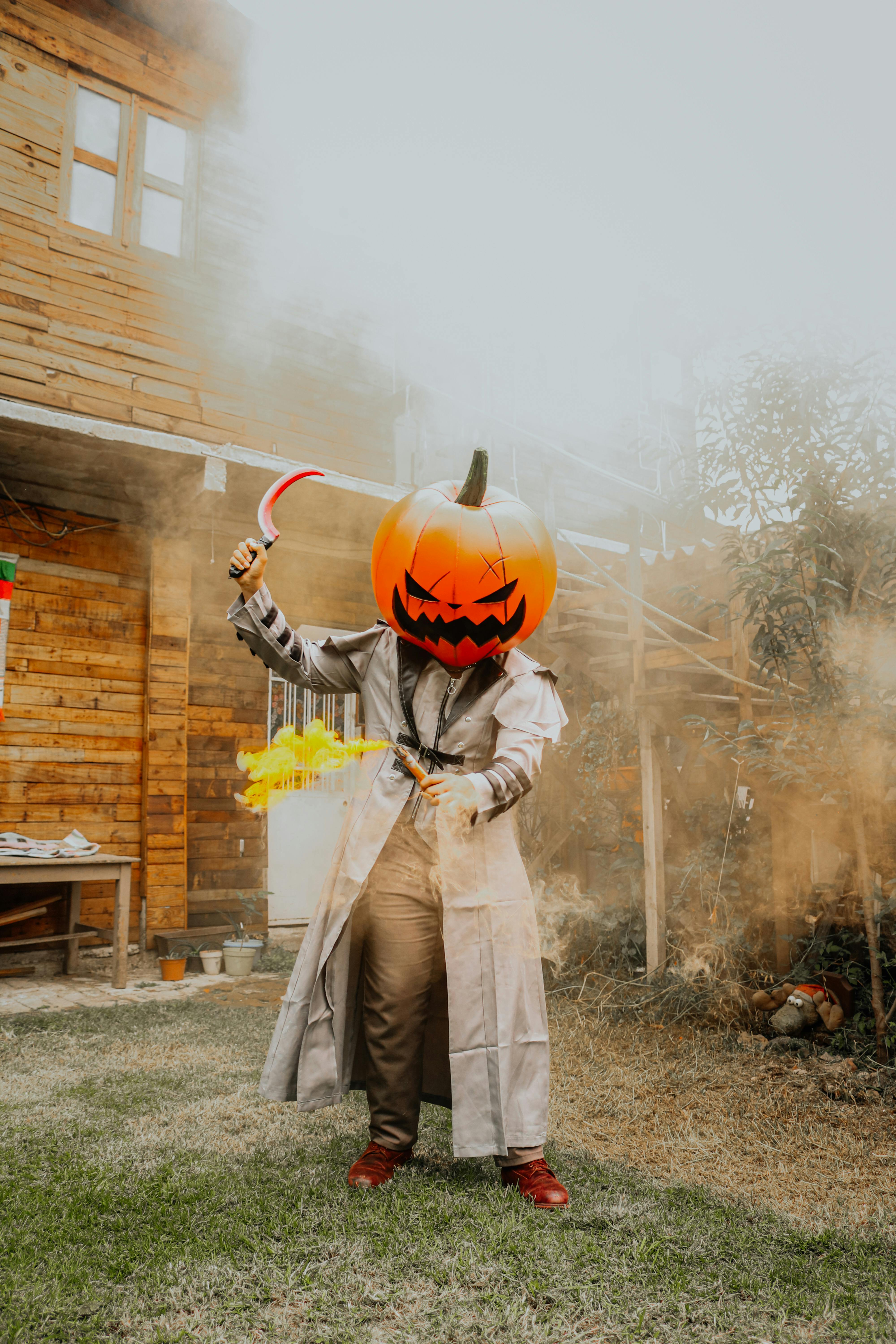 Halloween costume featuring a pumpkin head and scythe amidst fall decor.