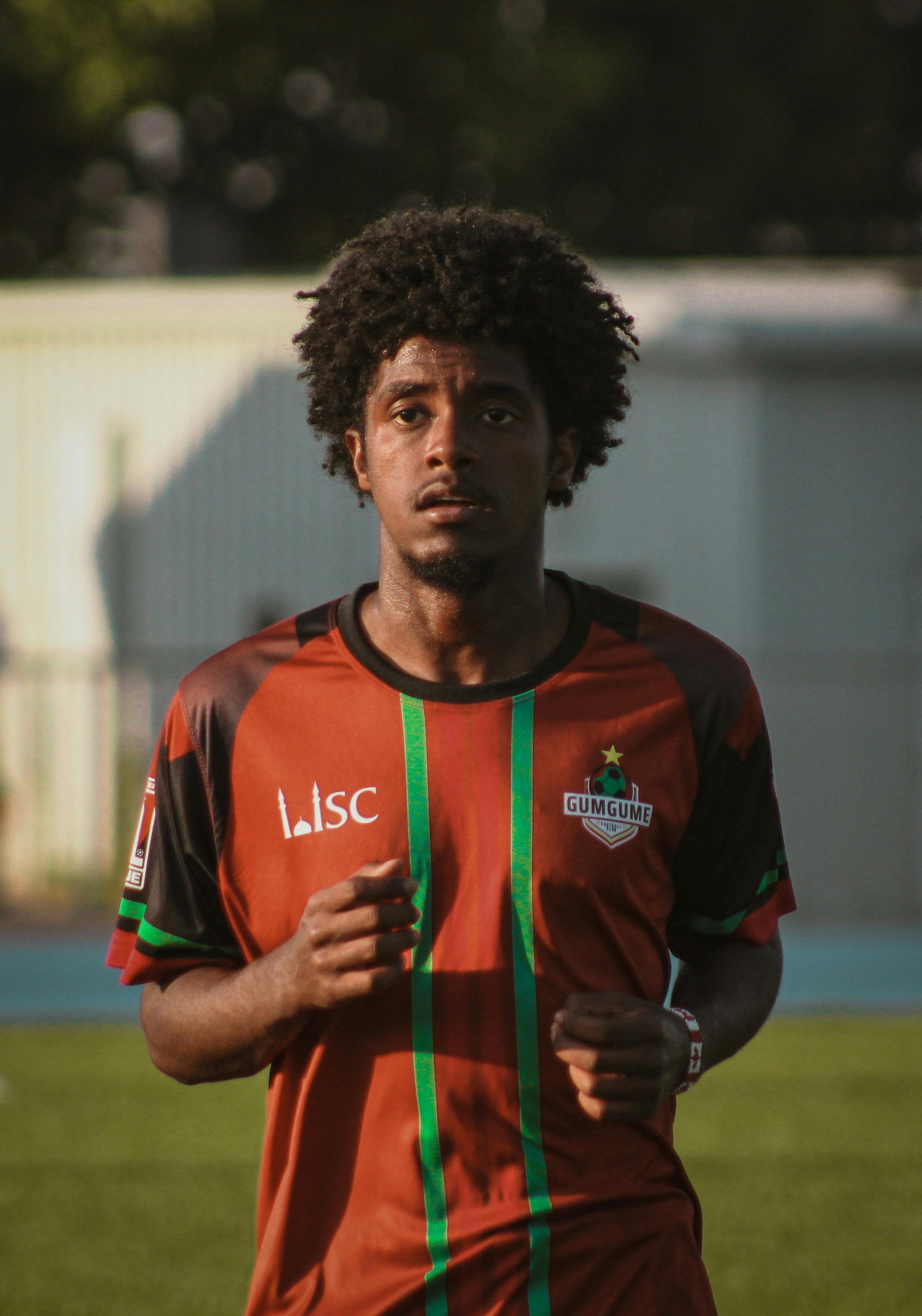 Focused young man wearing a sports jersey jogging on a sunny day outdoors.