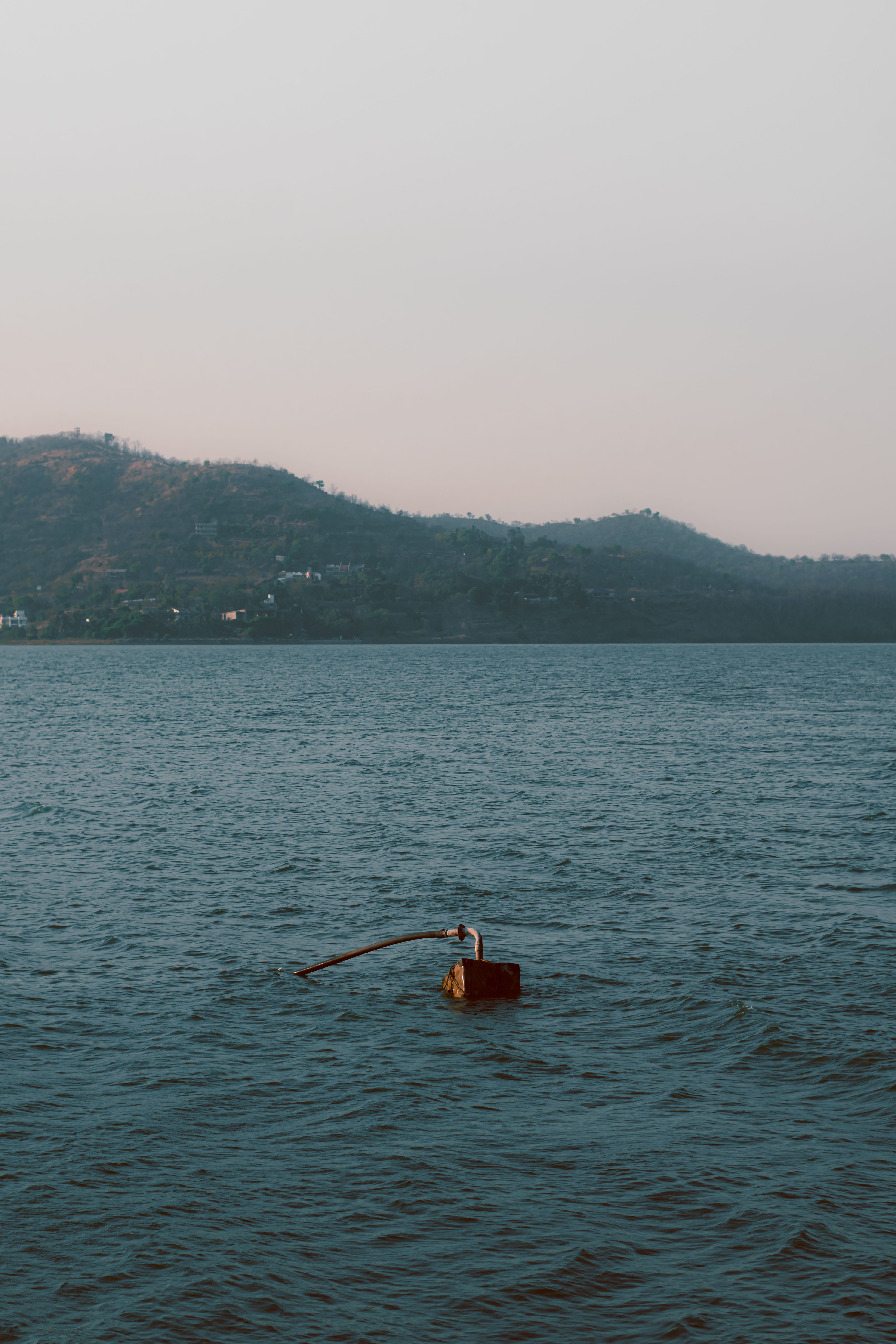 Calm waters with a buoy and hills in the distance, under a soft sky.