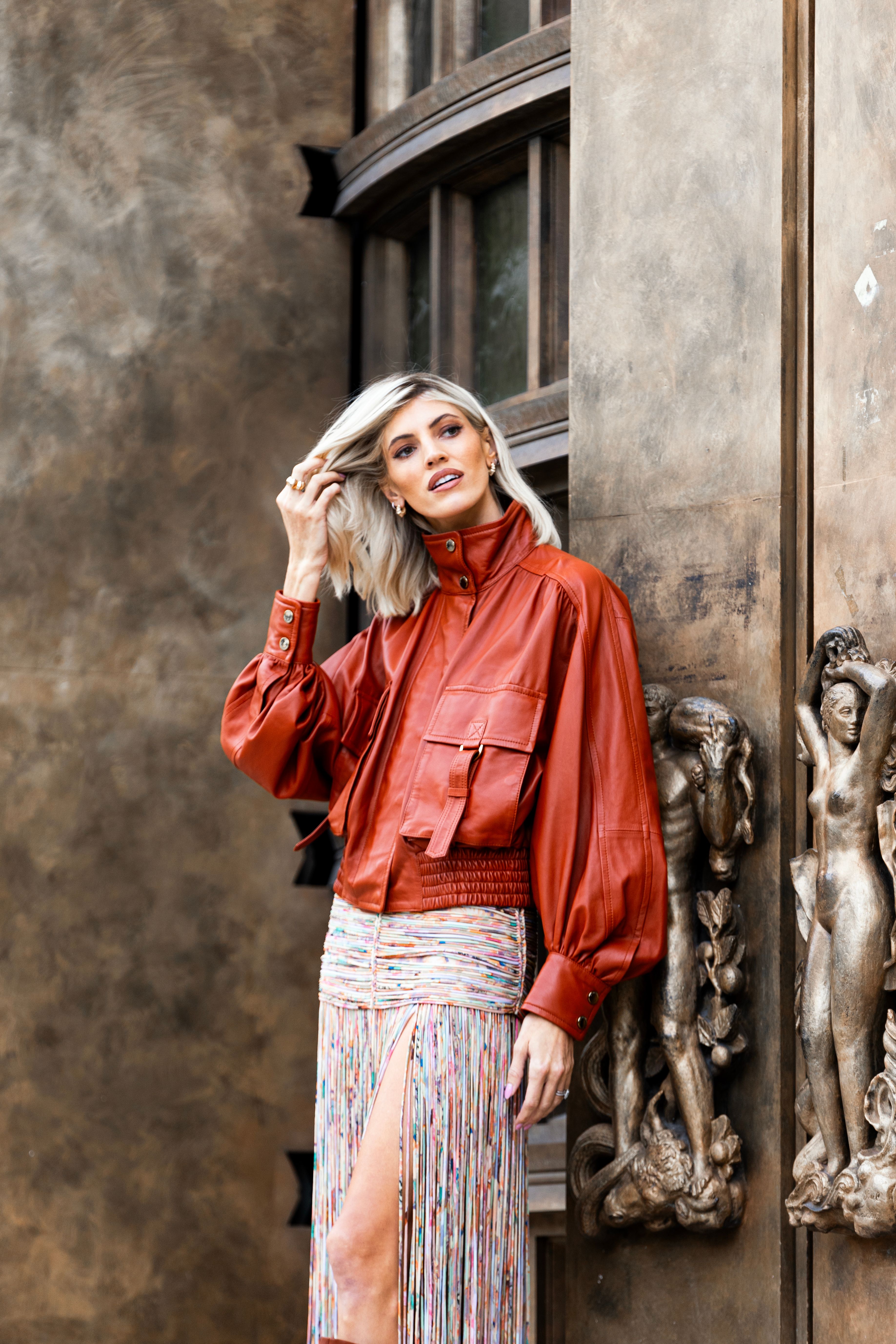 Stylish woman in red leather jacket posing by ornate sculptures, capturing urban elegance.