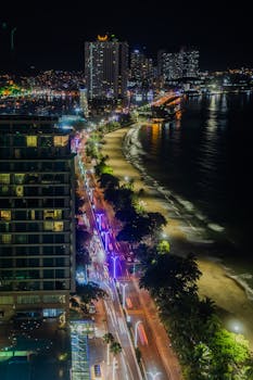 Stunning aerial view of a vibrant coastal city at night, showcasing illuminated streets and bustling beach life.