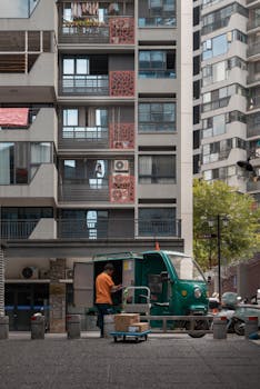 A delivery worker unloading a tricycle outside a residential building in the city.