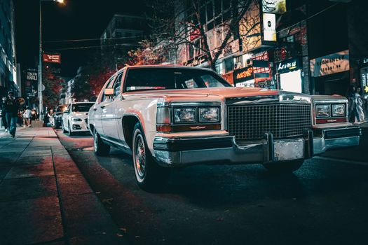 Classic car parked on a bustling city street at night, showcasing urban nightlife.