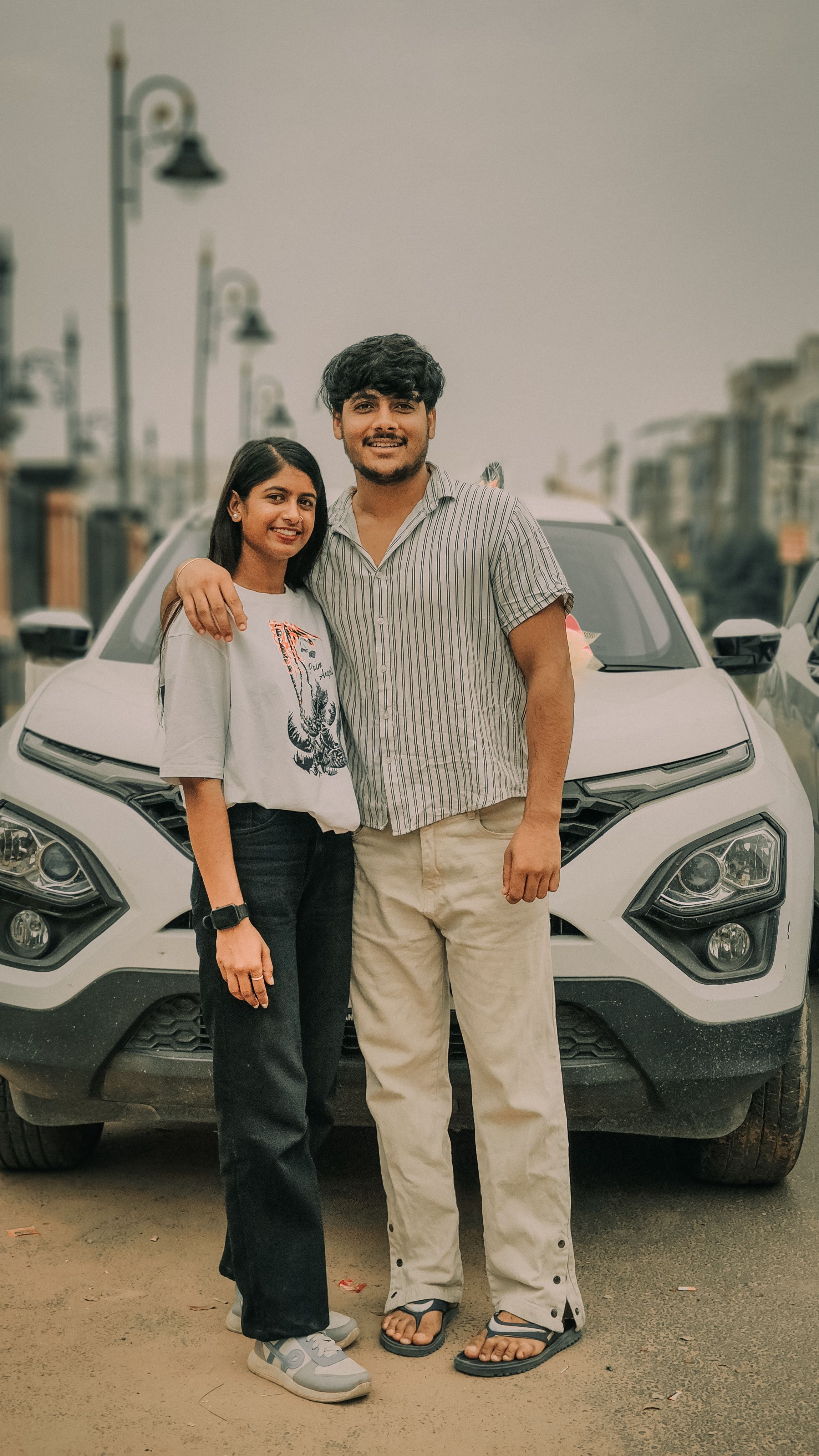 Happy couple posing by a car in a city street, capturing a joyful moment.