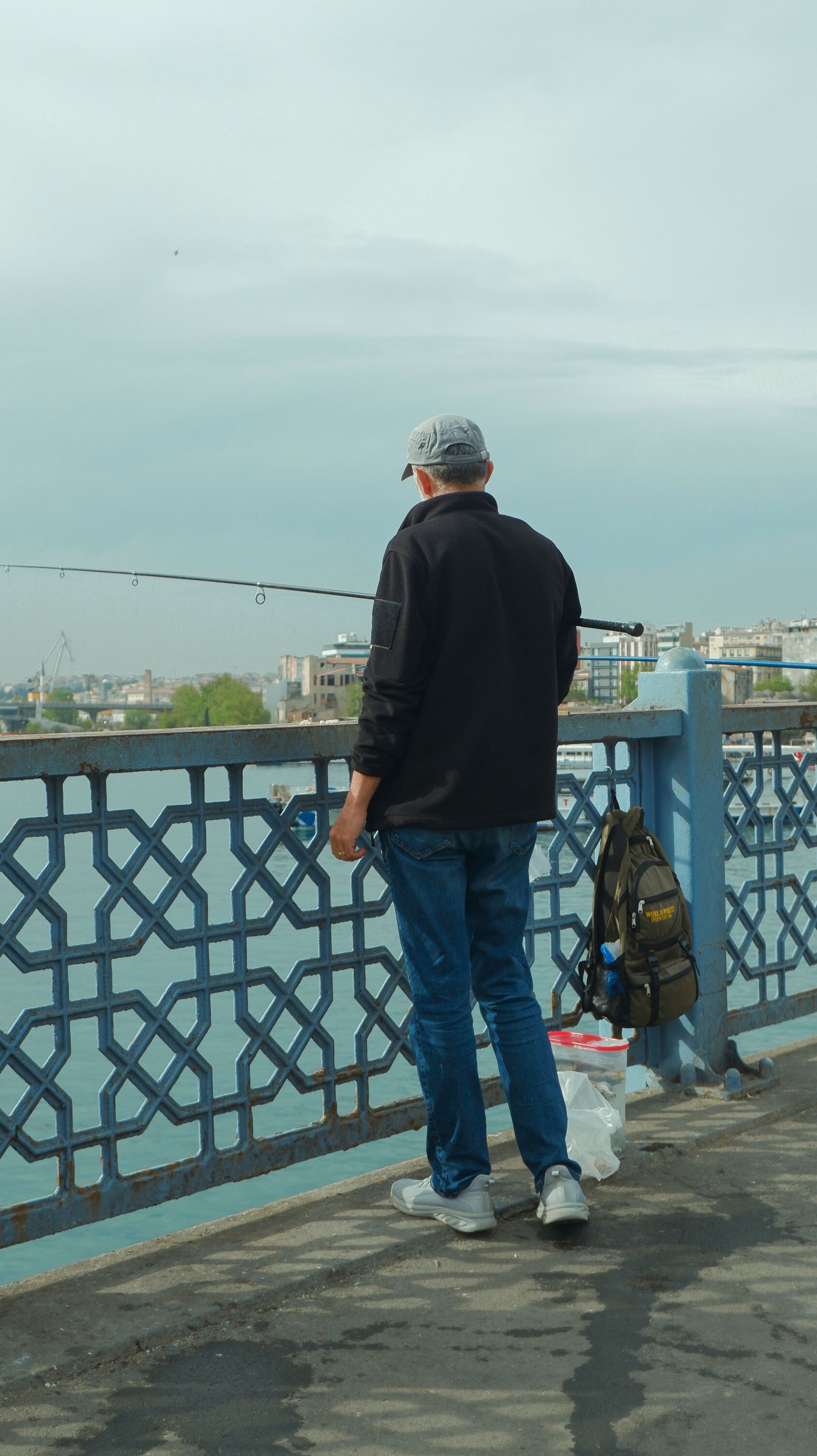 A man fishing on the Galata Bridge in Istanbul, Türkiye, with a scenic city backdrop.