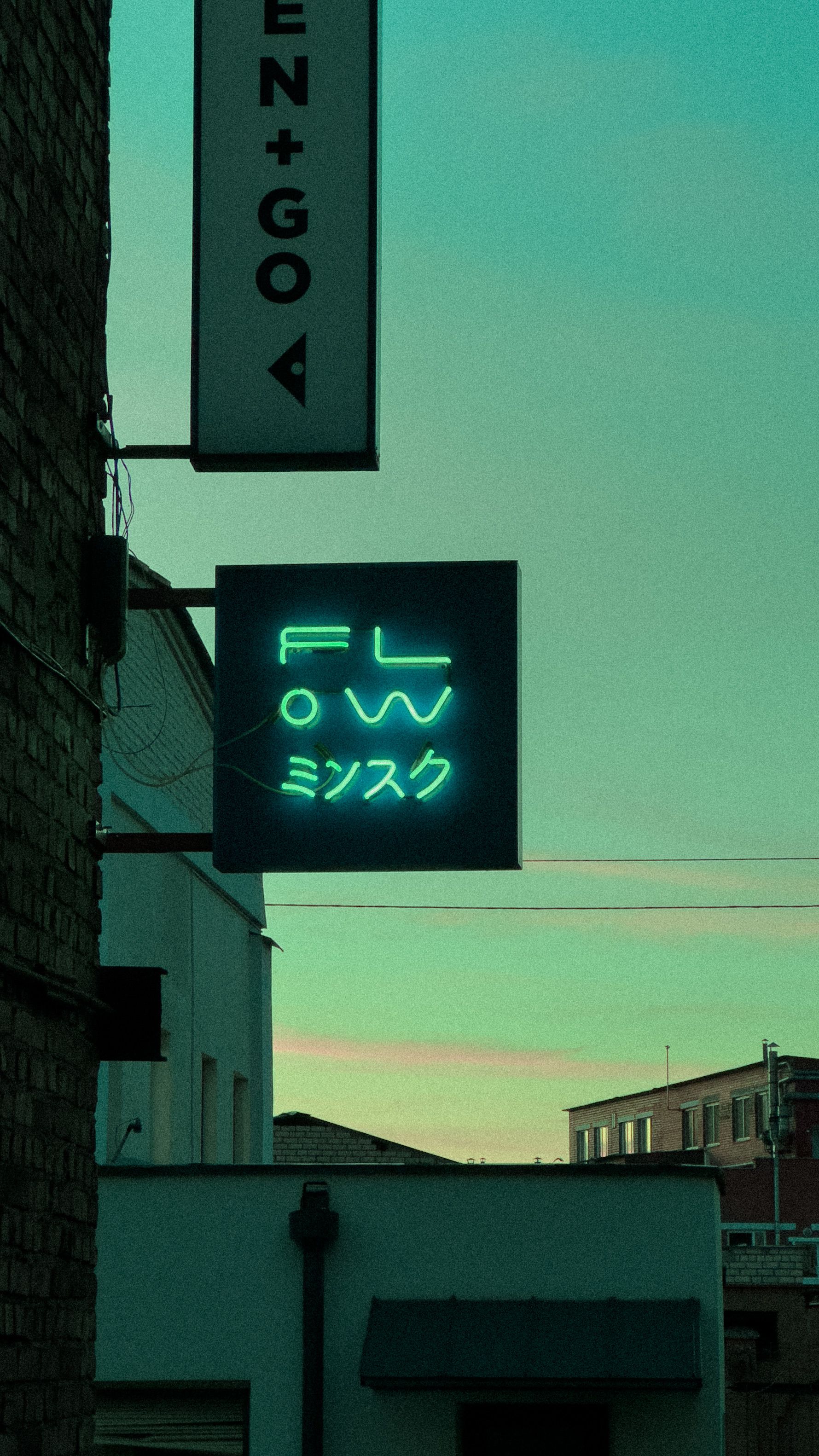 A vibrant neon sign illuminates an urban alleyway with a modern facade.