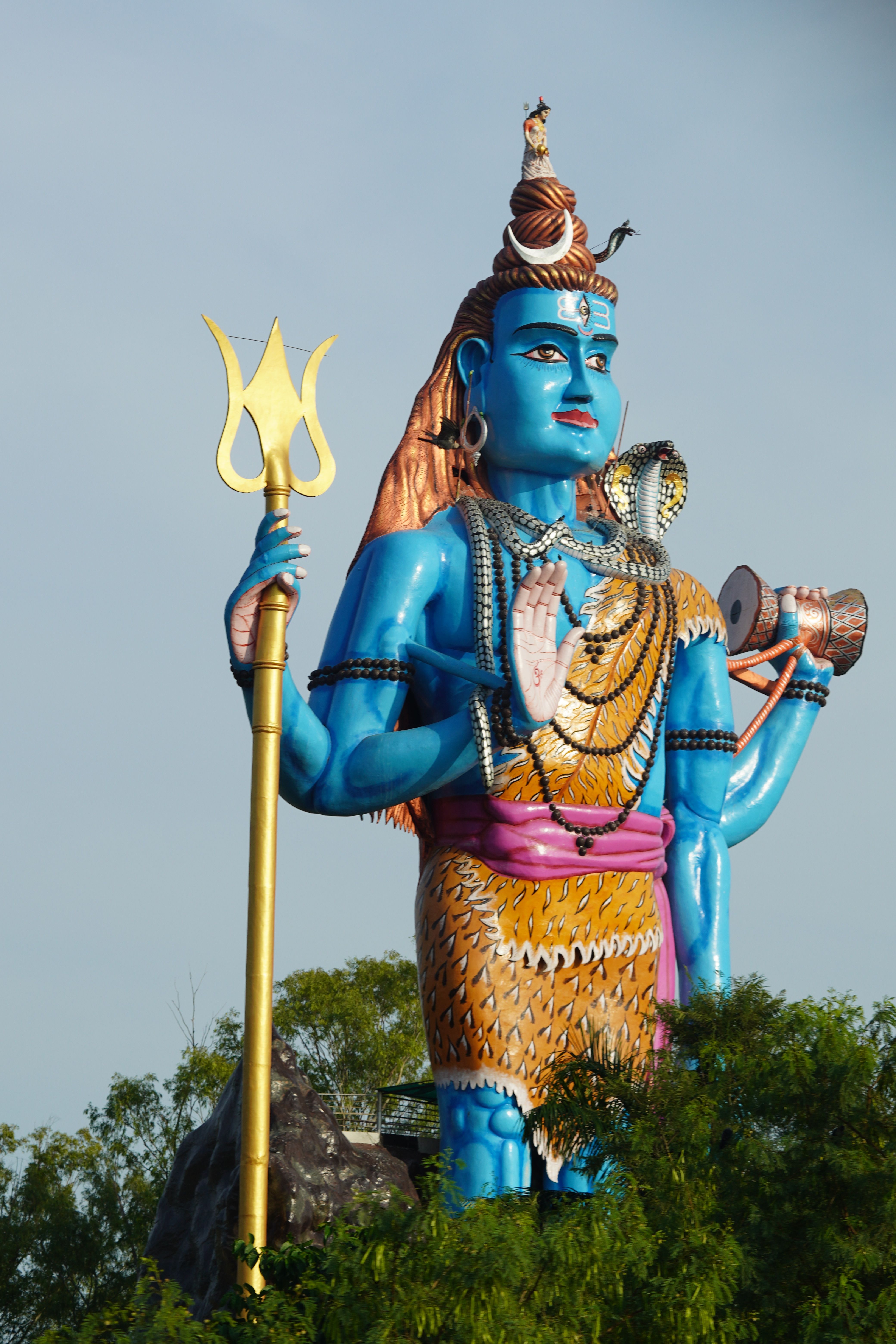 Majestic blue Shiva statue holding a trident, surrounded by greenery.