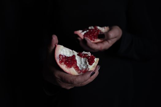 Close-up of hands holding a fresh pomegranate in dark lighting.