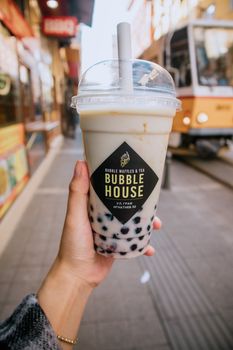 Close-up of hand holding bubble tea with city street background, featuring tram.
