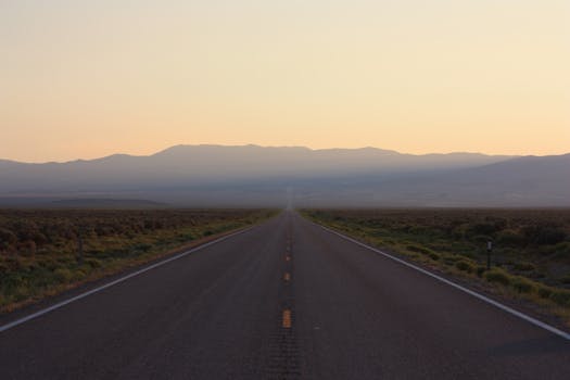A long empty highway stretching towards misty mountains under a sunset sky.