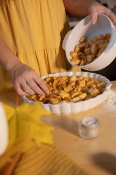 Woman preparing apple pie filling in a white dish, perfect for fall baking.