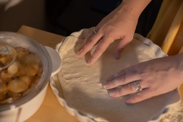 Hands shaping dough in a pie dish next to apple filling, ready to bake.