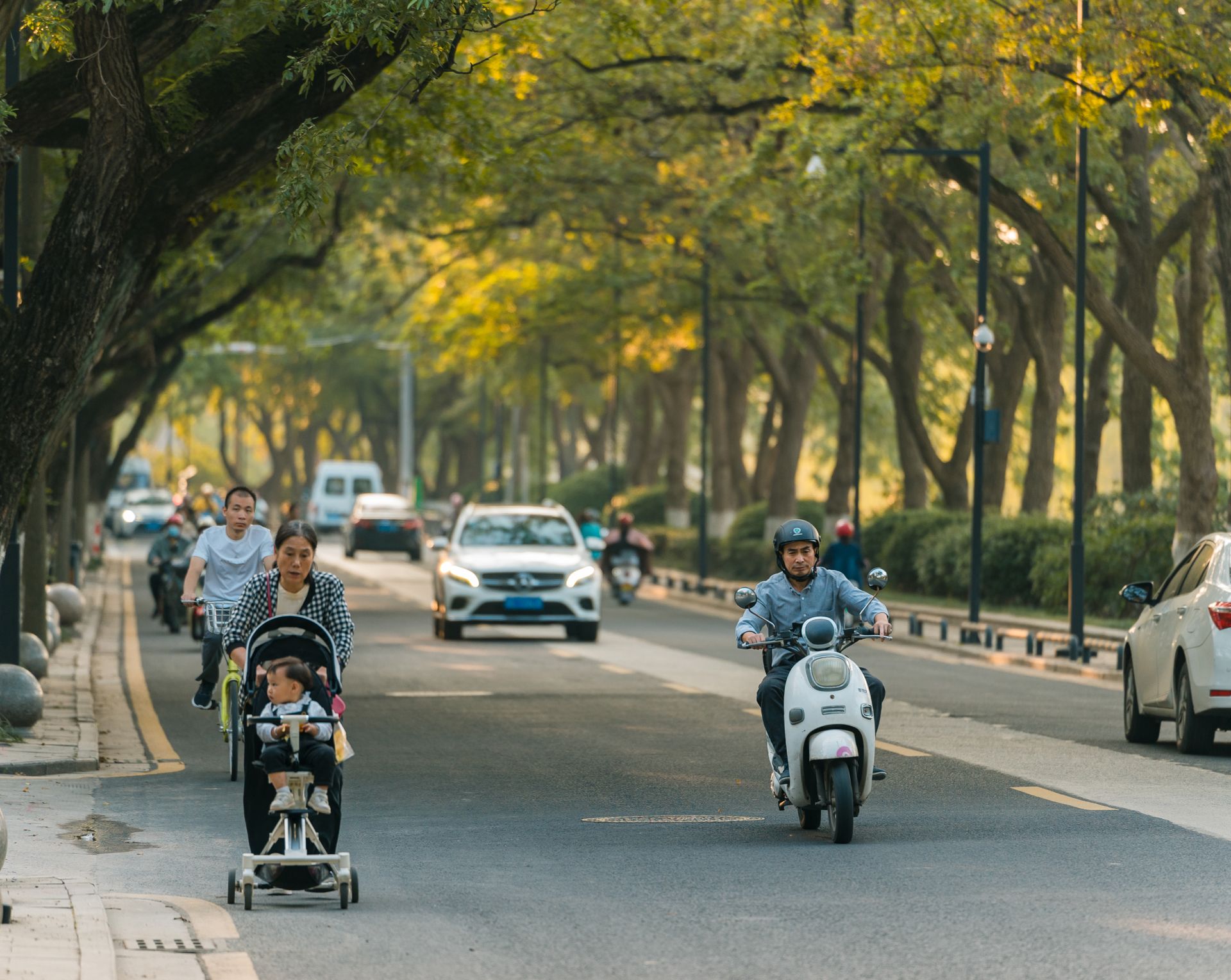 Daily life on a street in Suzhou with people on scooters, bicycles, and cars.