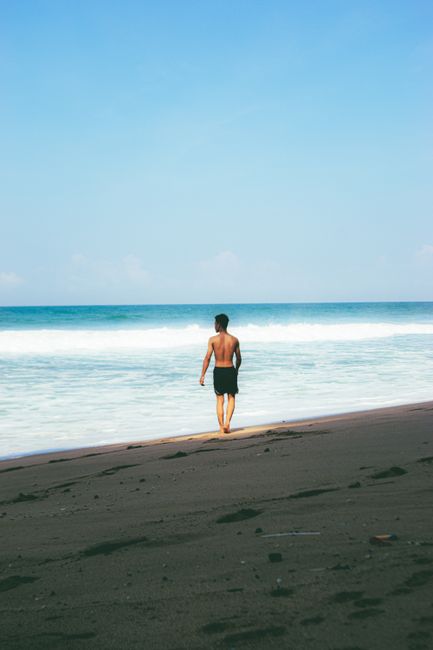 Silhouette of a man walking on Parangtritis Beach, Yogyakarta, Indonesia, under a clear blue sky.