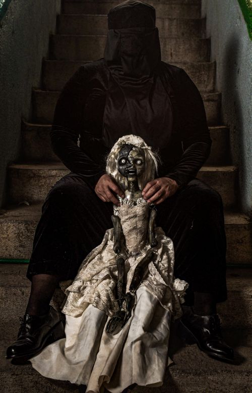 Free A mysterious figure holding a gothic doll on dimly-lit stairs, evoking a haunting atmosphere. Stock Photo