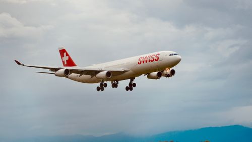 Free Swiss airplane flying against a backdrop of cloudy sky, showcasing aviation and travel. Stock Photo