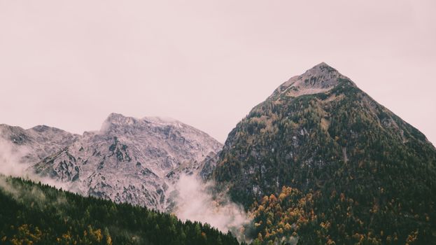 Majestic mountain range in Tyrol, Austria with autumn foliage and misty clouds.