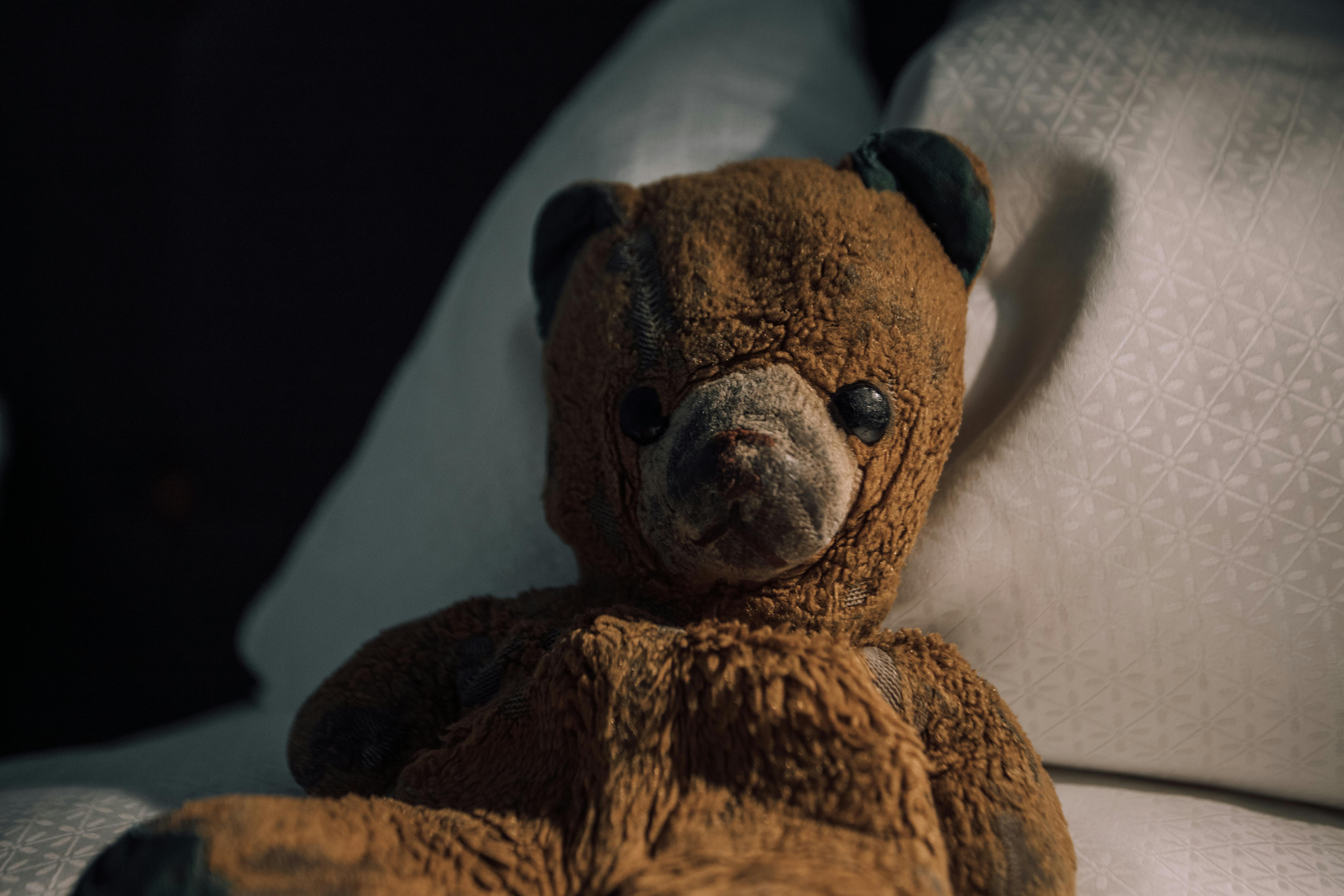 A charming vintage teddy bear sitting on a bed in a cozy room, evoking nostalgia.