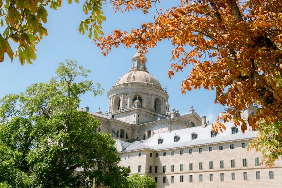 Impresionante vista del Monasterio de El Escorial en Madrid enmarcada por vibrantes hojas de otoño.