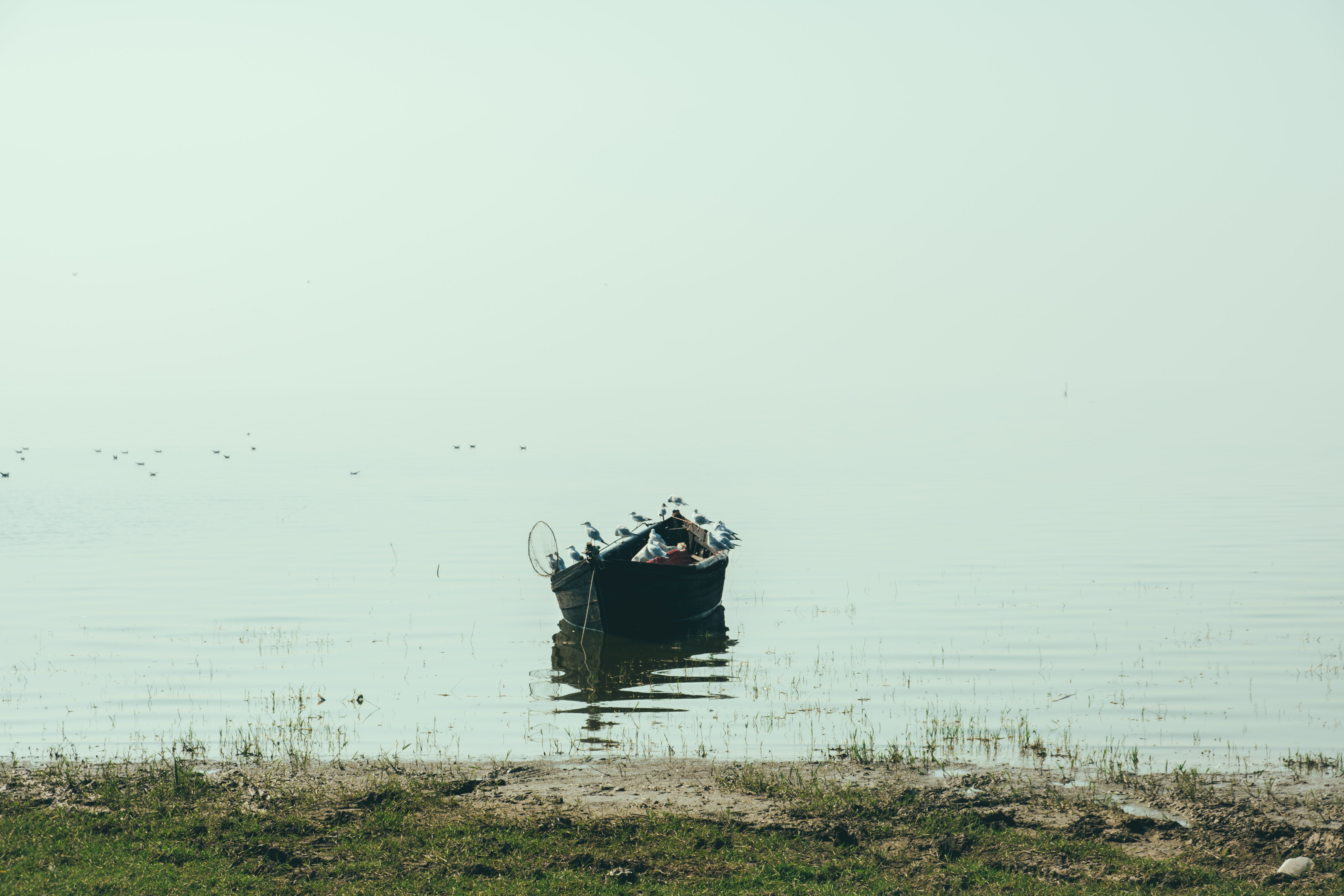A serene scene of a lone boat on a calm, misty lake during the day, evoking peace.
