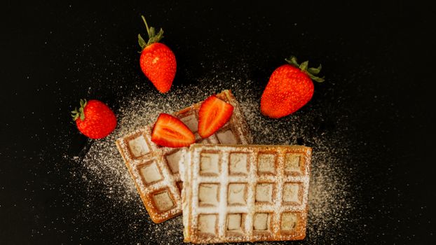 Close-up of crispy waffles with fresh strawberries on dark background.