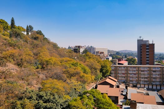 Aerial view of urban buildings nestled against a hillside with lush greenery.