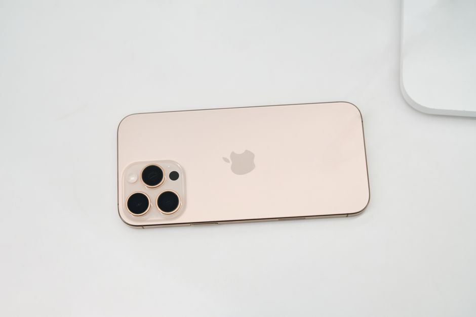 Gold smartphone featuring a triple-lens camera setup placed on a clean white surface.