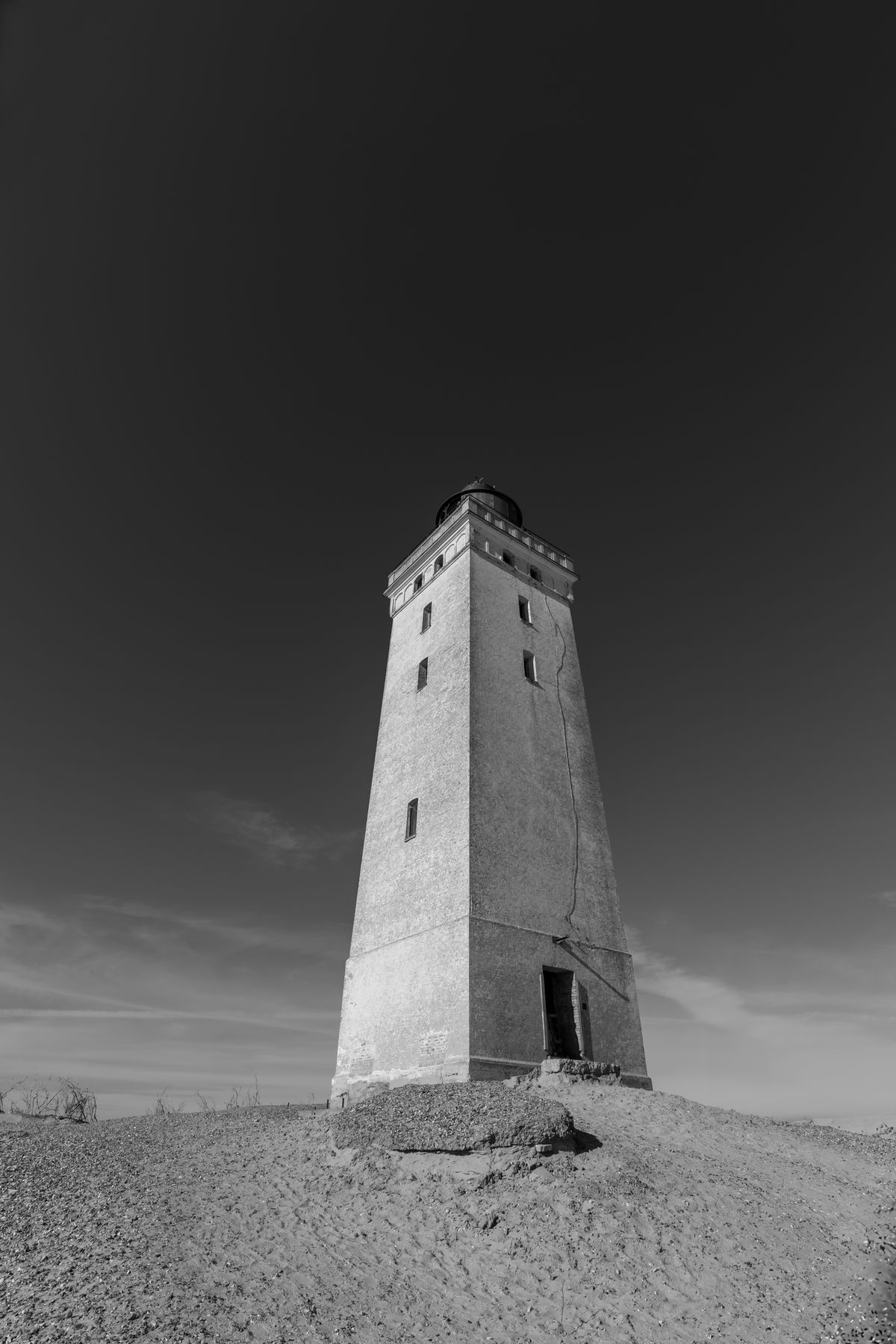 Weathered lighthouse tower on a sand dune in black and white