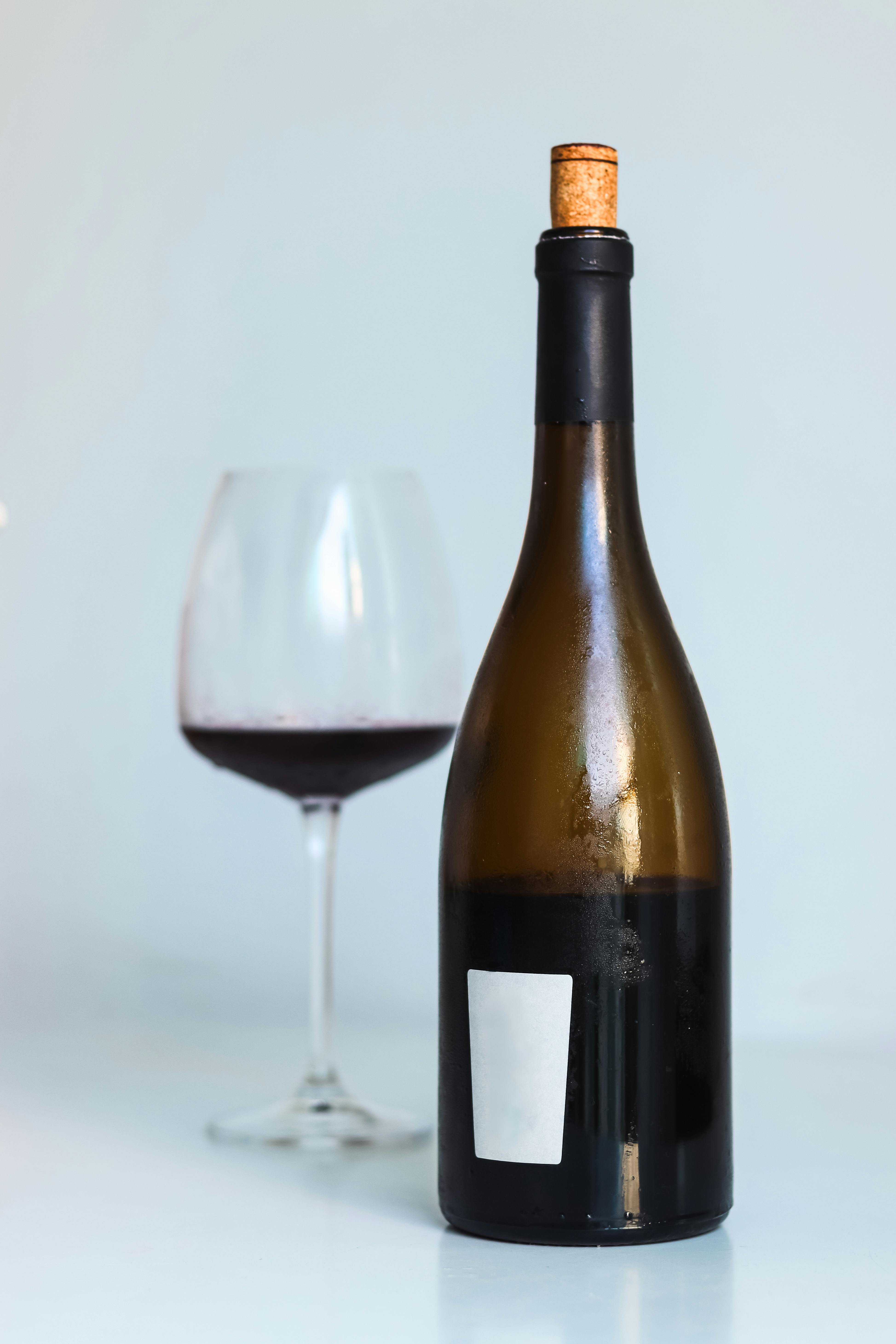 A minimalist composition featuring a bottle of red wine with a cork and a wine glass on a clean background.