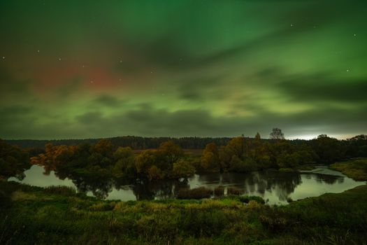 A stunning aurora borealis above a serene night landscape with a reflective river.