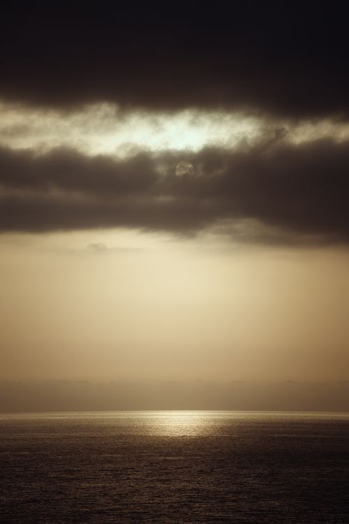 Free Experience tranquility with a serene ocean view at sunset, featuring dramatic clouds and golden reflections. Stock Photo