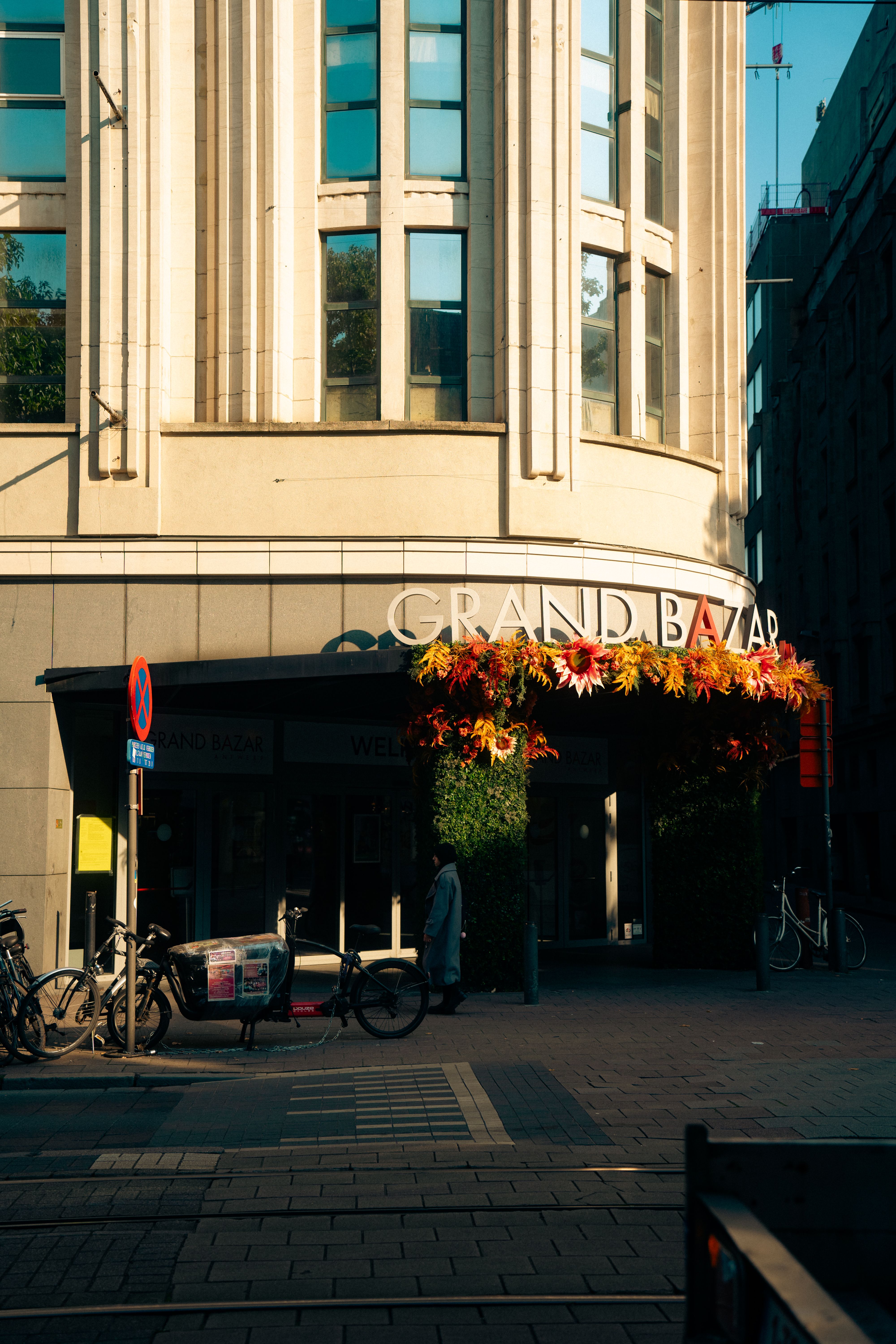 Street view of the Grand Bazar entrance in Antwerp, lit by warm sunlight. Bicycles under autumn decor.