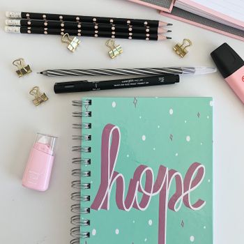 Flat lay of pink and teal desk supplies with a hope-themed notebook, inspiring productivity.（イメージ）