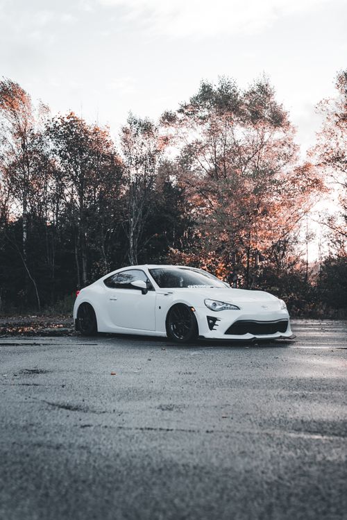 Free A white sports car parked on a road surrounded by autumn trees, capturing a seasonal blend of nature and technology. Stock Photo