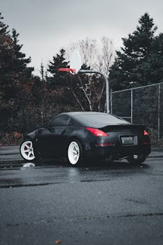 Black sports car parked in an empty urban basketball court surrounded by dense trees.
