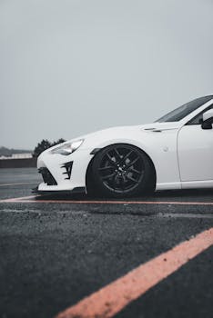 Close-up of a stylish white sports car parked on a wet asphalt road in rainy weather.