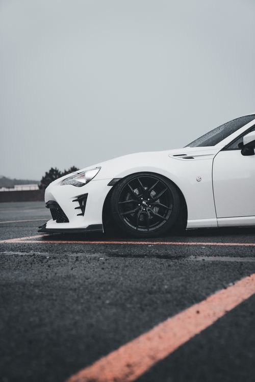 Free Close-up of a stylish white sports car parked on a wet asphalt road in rainy weather. Stock Photo