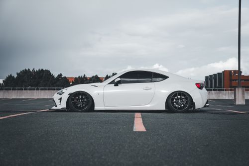 Free White sports car parked in an empty urban lot with a cloudy sky in the background. Stock Photo