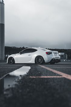 A stylish white sports car parked on an outdoor lot, reflecting on the wet surface.