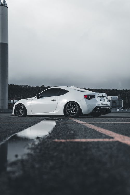 Free A stylish white sports car parked on an outdoor lot, reflecting on the wet surface. Stock Photo