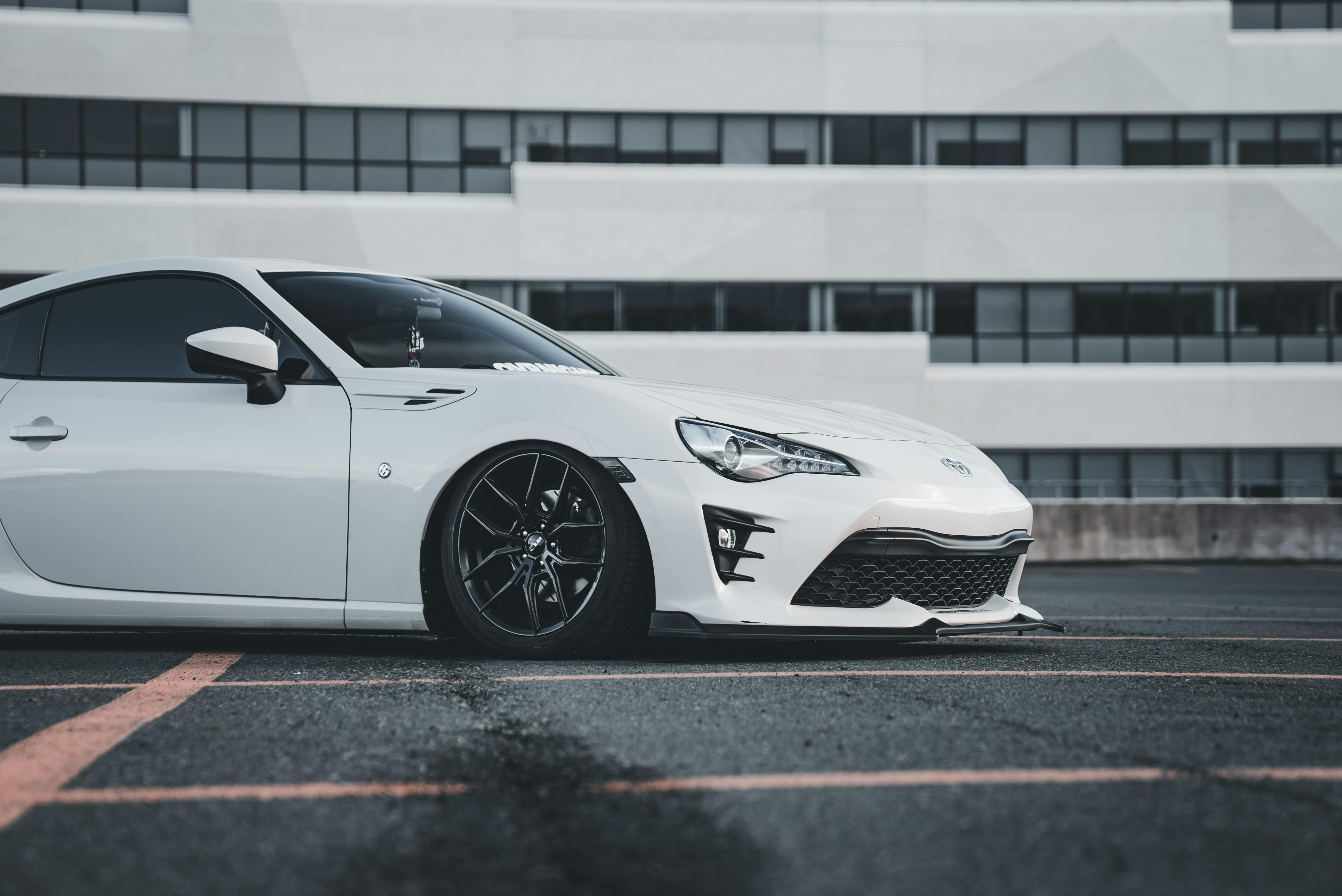 White sports car parked in front of a modern building with black wheels and tinted windows.