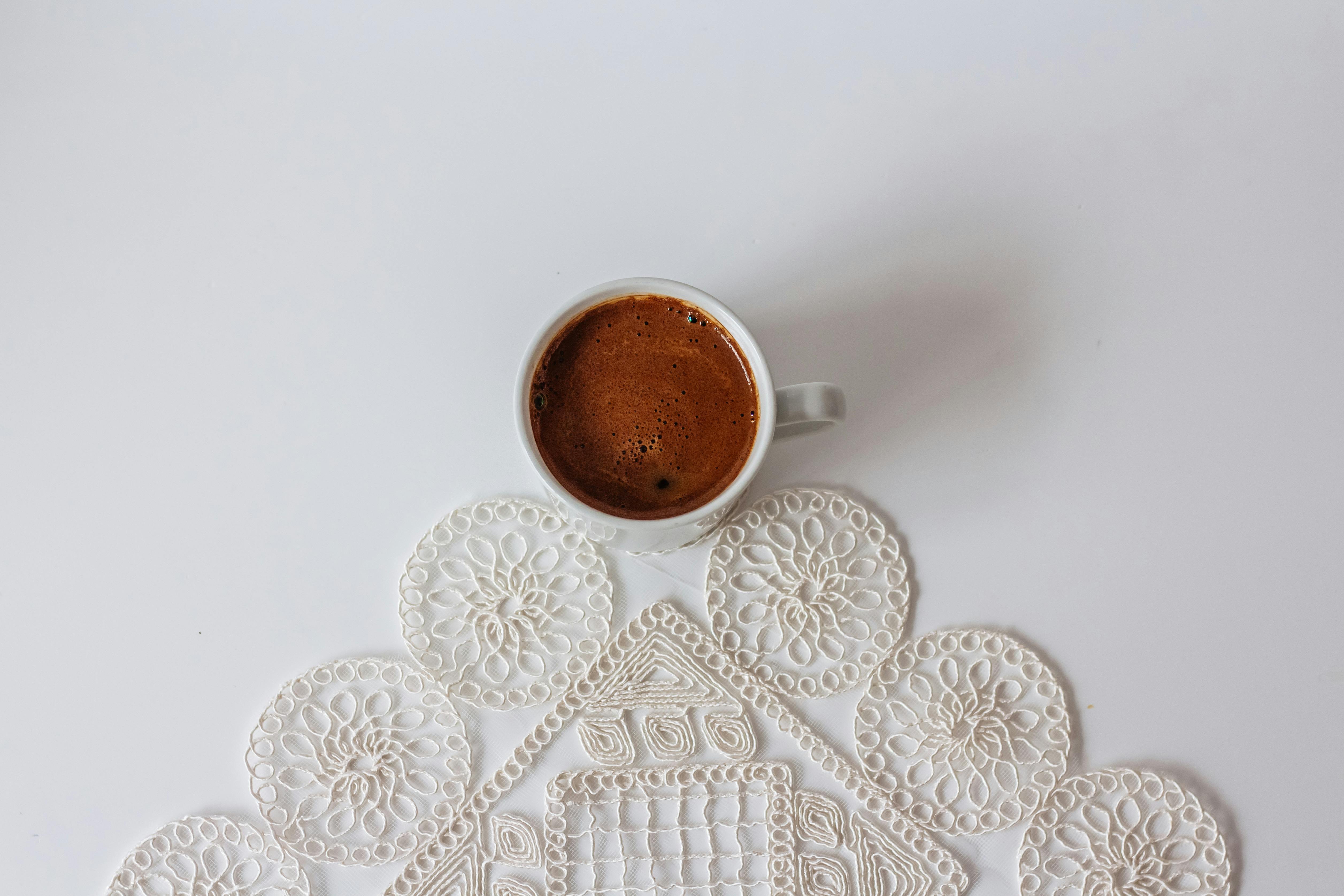 Simple white coffee cup on a crochet doily against a clean backdrop.