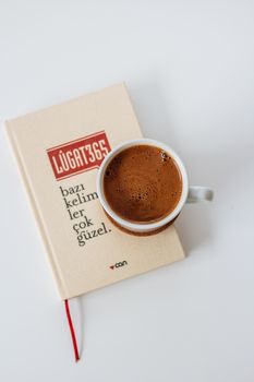 A cup of coffee rests on a Turkish book on a white surface, offering a cozy vibe.