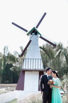 在风车前，新娘和新郎相拥，捕捉浪漫的婚礼时刻