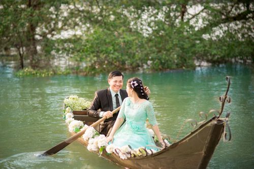 Free Happy couple in elegant attire rowing a boat adorned with flowers on a picturesque lake. Stock Photo