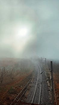 Moody view of railway tracks disappearing into dense fog under overcast skies.