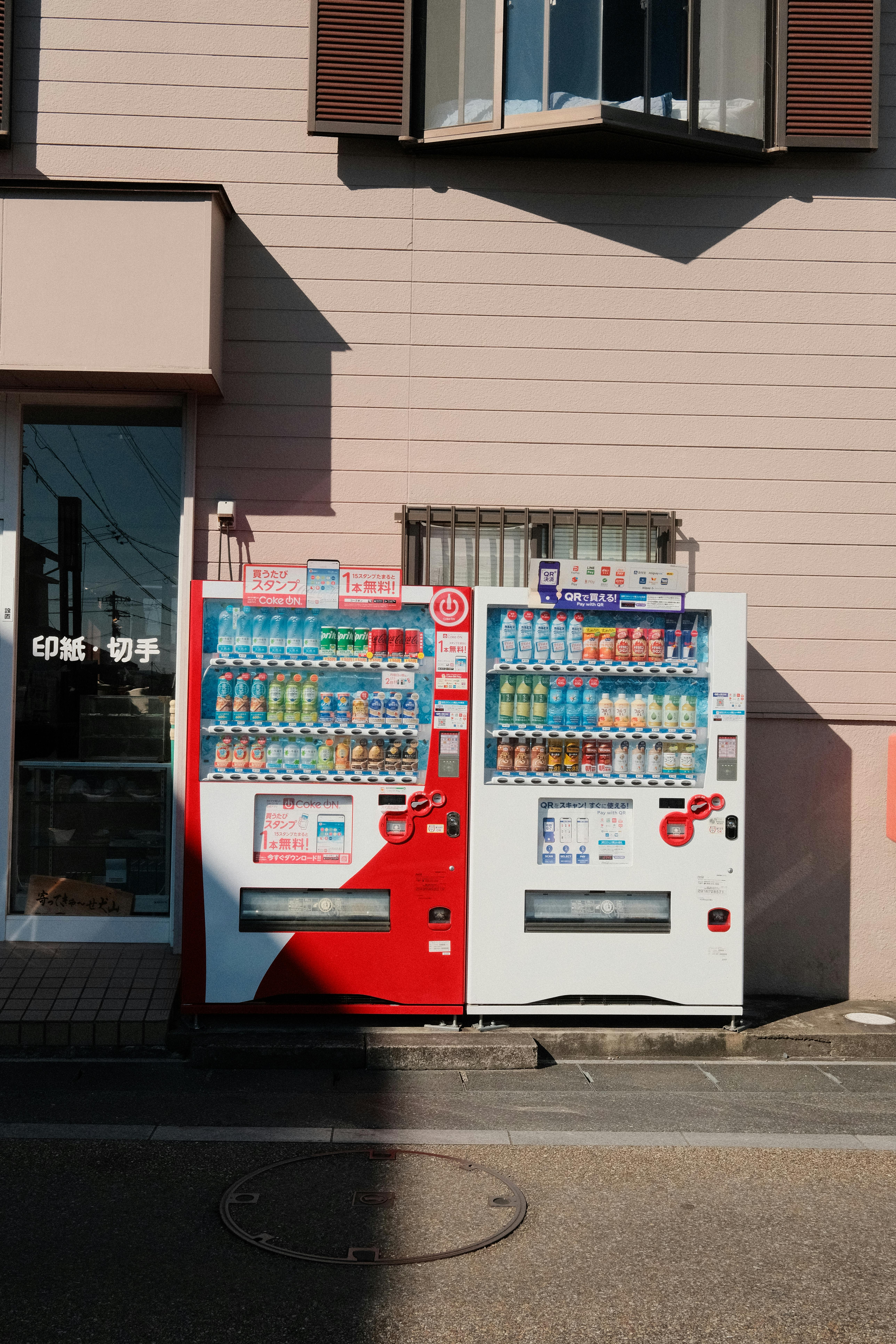 Two colorful vending machines under sunlight in Inuyama, showcasing diverse drink options.